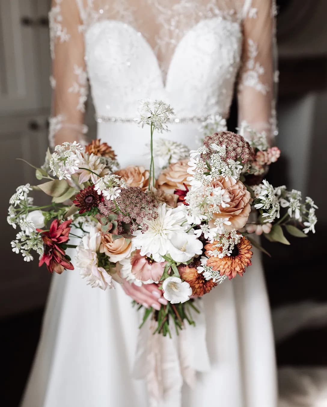 Bride in lace wedding dress holds autumn wedding flower bouquet