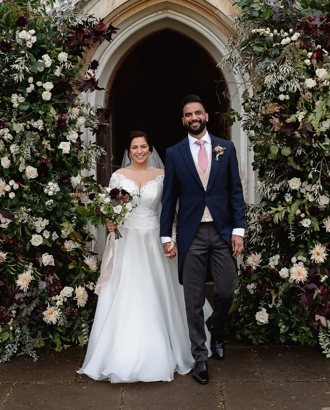 Bride and groom leave their wedding ceremonu surrounded by floral arch