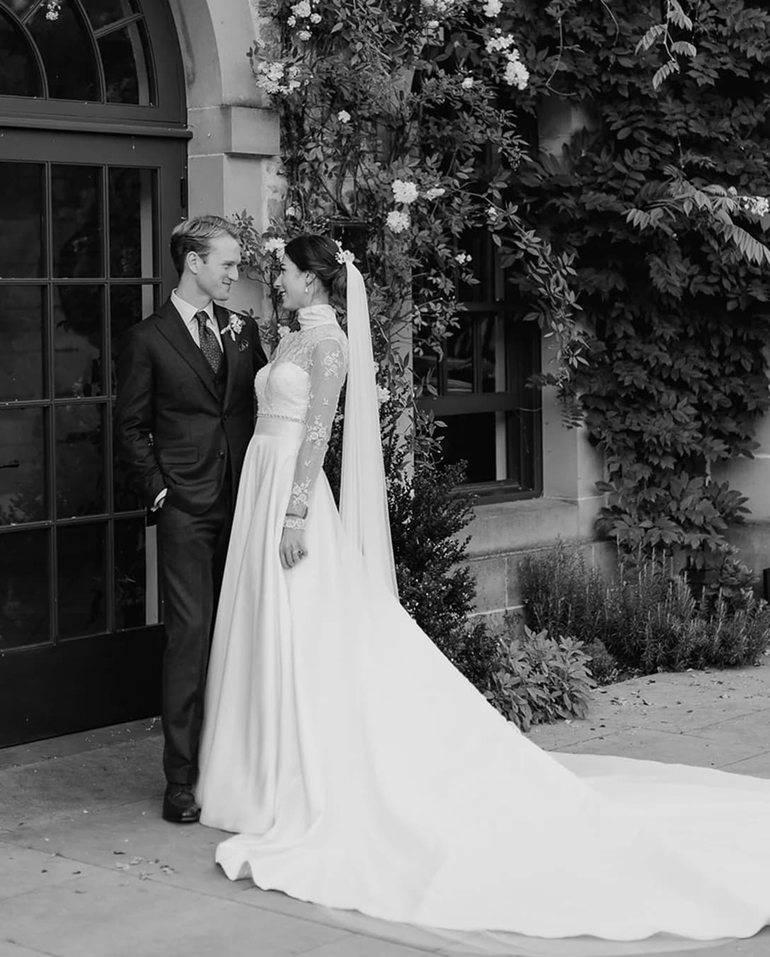 Bride and groom pose next to a wall covered in foliage