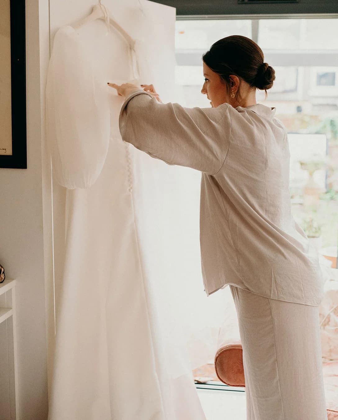 Bride prepares her bridal dress that's hanging on window