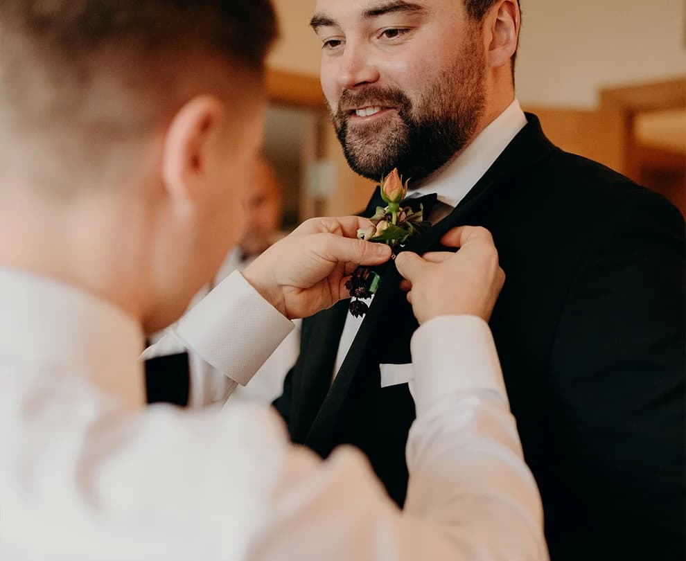 Groom getting his boutonniere fixed by his groomsman
