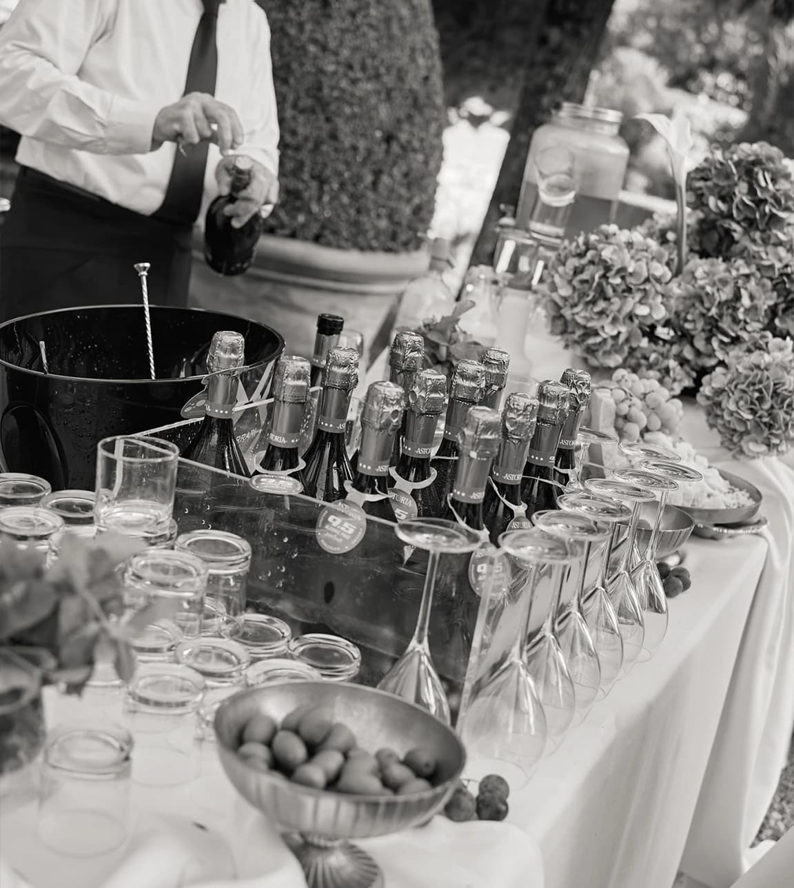 Wedding drinks station with chilled champagne bottles, glassware, and a bartender pouring, styled with floral accents and fresh garnishes.