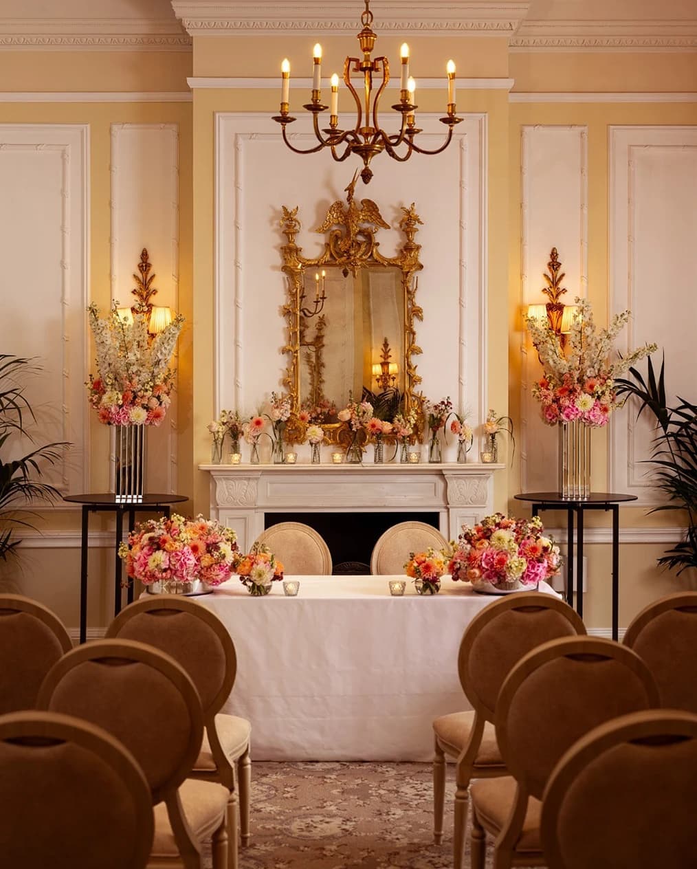 Elegant wedding ceremony setup at The Savoy London with floral arrangements, fireplace backdrop, and chandelier-lit room