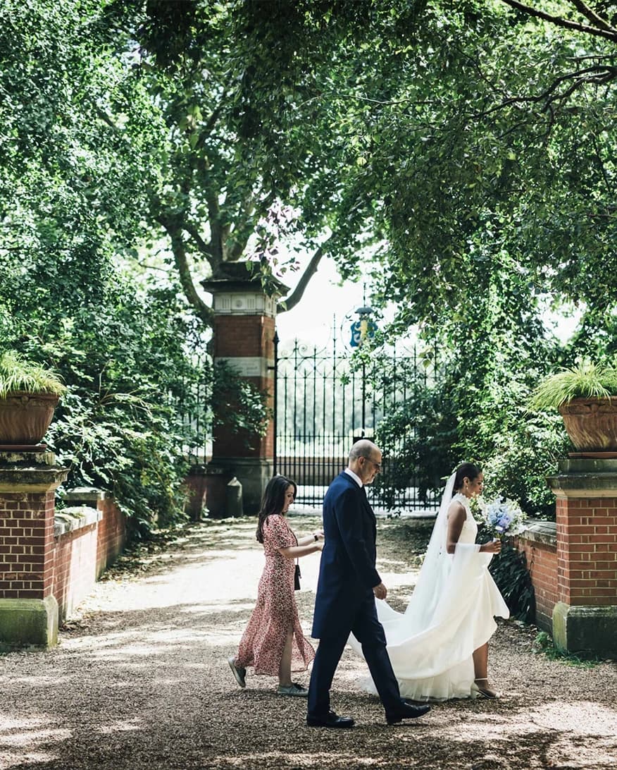 Bride walking through Chelsea Physic Garden London near embankment gate with greenery and historic entrance