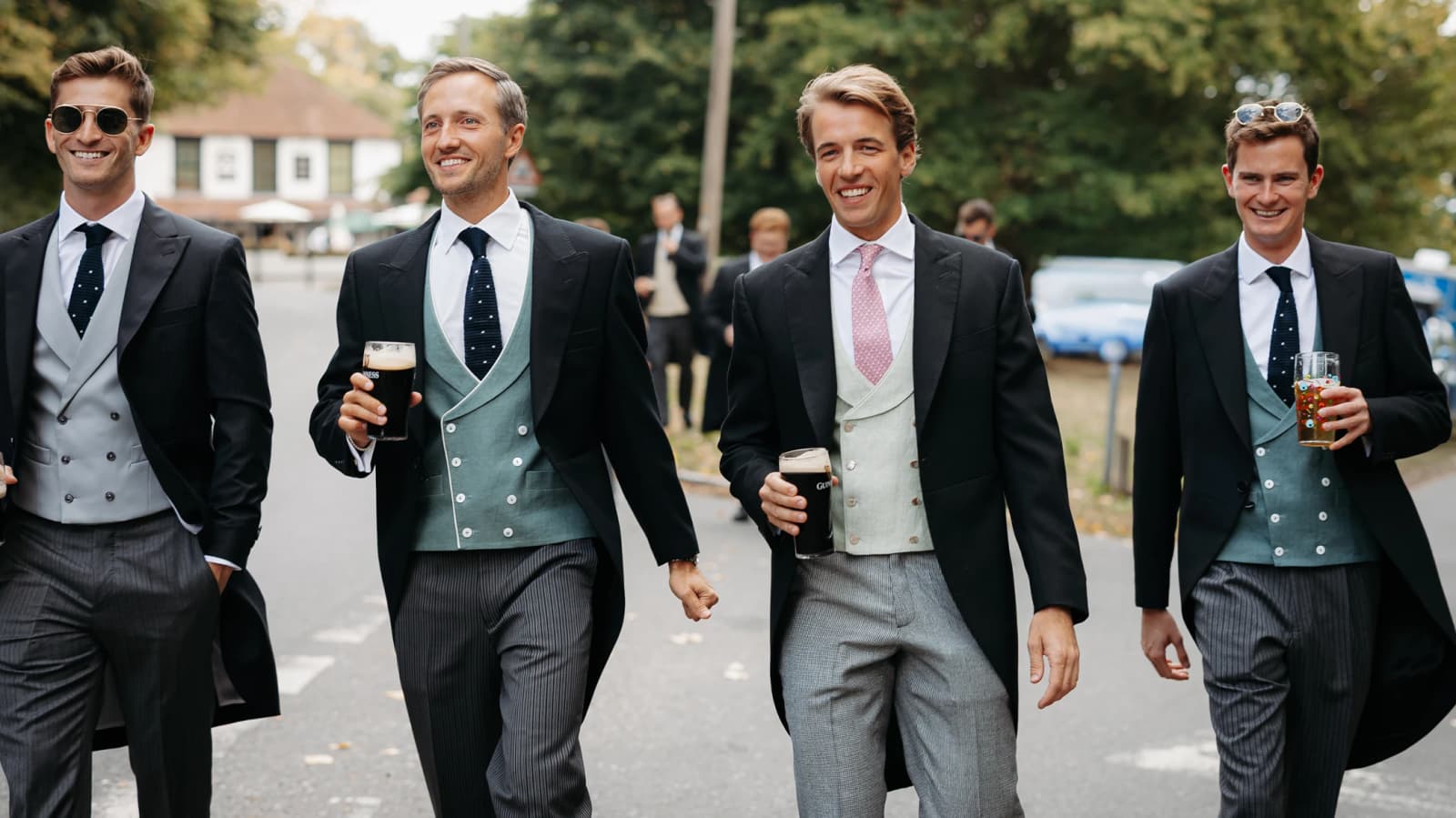  Groom and groomsmen wearing matching morning suits and ties, arriving from the ushers' lunch ahead of a English countryside wedding.