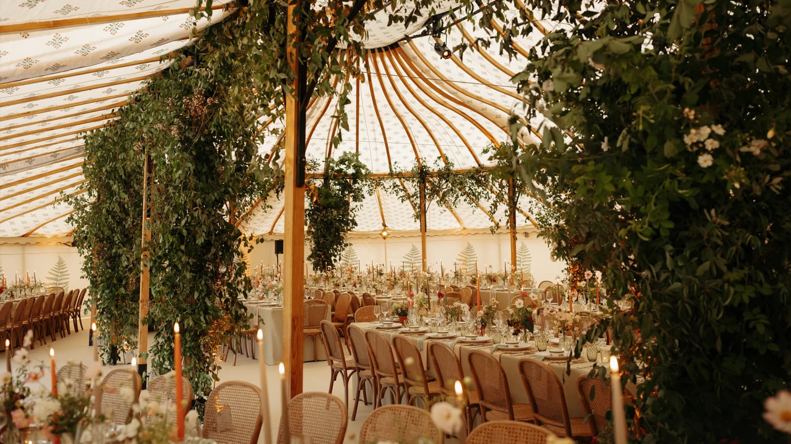 Luxury sailcloth marquee decorated with suspended greenery, foliage-covered supports, soft candlelight and refined floral tablescapes for an English countryside wedding.
