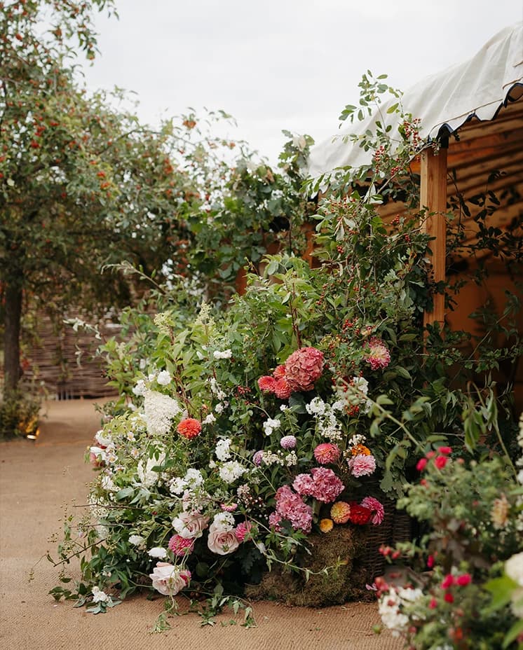 Abundant floral installation featuring seasonal dahlias, hydrangeas, roses and cascading greenery decorating the entrance to a luxury wedding marquee