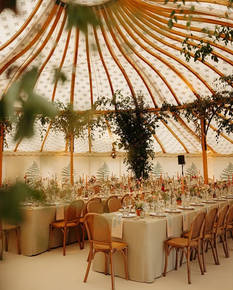 Luxury sailcloth wedding marquee featuring cascading greenery installations, elegant tablescapes, rattan chairs and abundant floral arrangements for a countryside wedding reception.