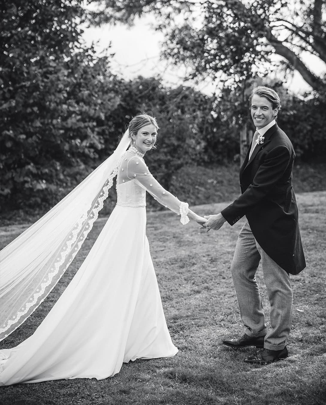Bride and groom holding hands and sharing a joyful moment in a garden during their countryside wedding