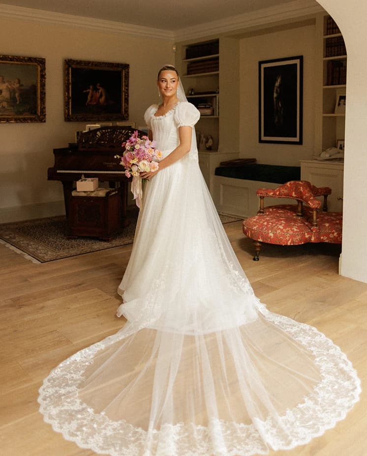 Bride in a romantic puff-sleeve wedding dress with a lace-edged veil, holding a pink bridal bouquet during bridal portraits before her English countryside wedding.