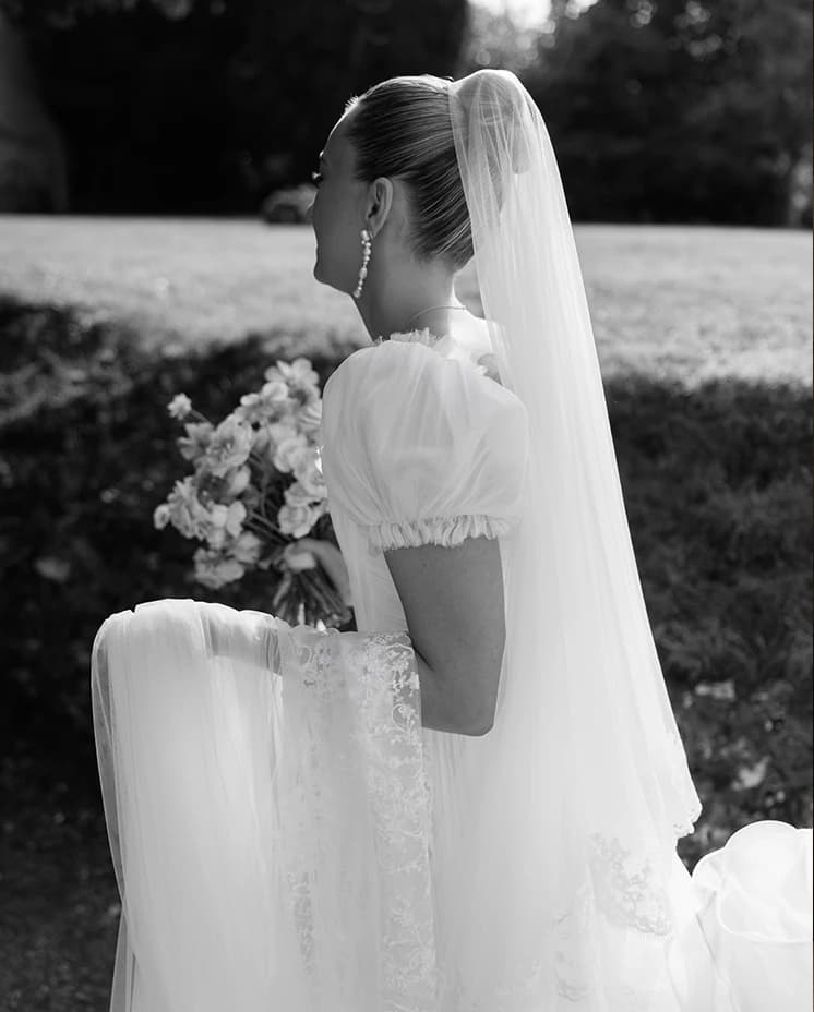 Bride in a romantic puff-sleeve wedding dress with a lace-edged veil and bouquet, captured in an elegant black and white bridal portrait before her countryside wedding.