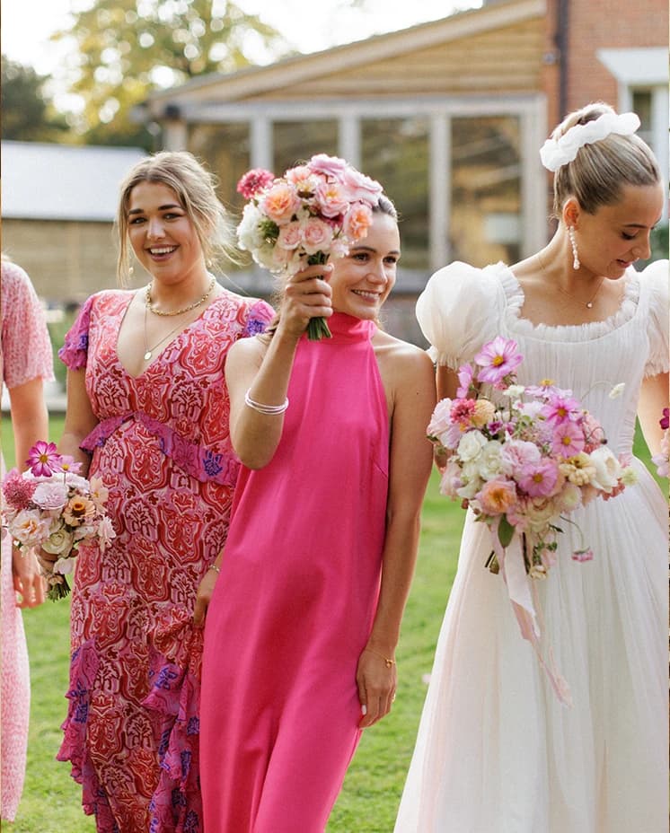 Bride and bridesmaids holding pink and blush bouquets during an English countryside wedding reception, celebrating together in elegant pink dresses and romantic bridal style.
