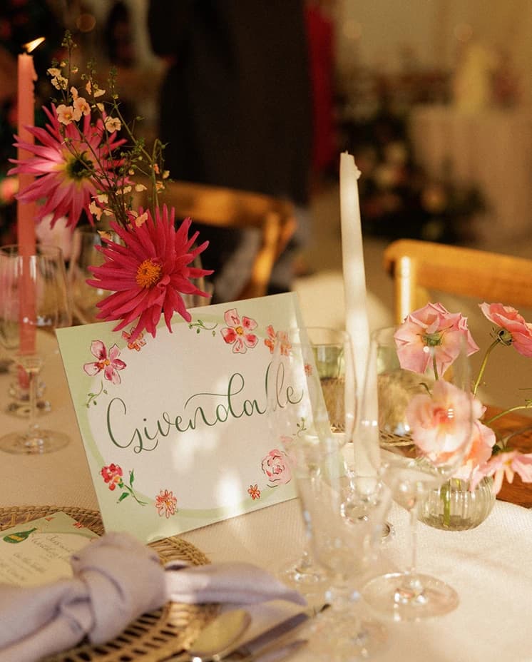 Elegant wedding reception table with handwritten table name card, pink floral centrepieces and candlelit styling inside a sailcloth marquee at an English countryside wedding.