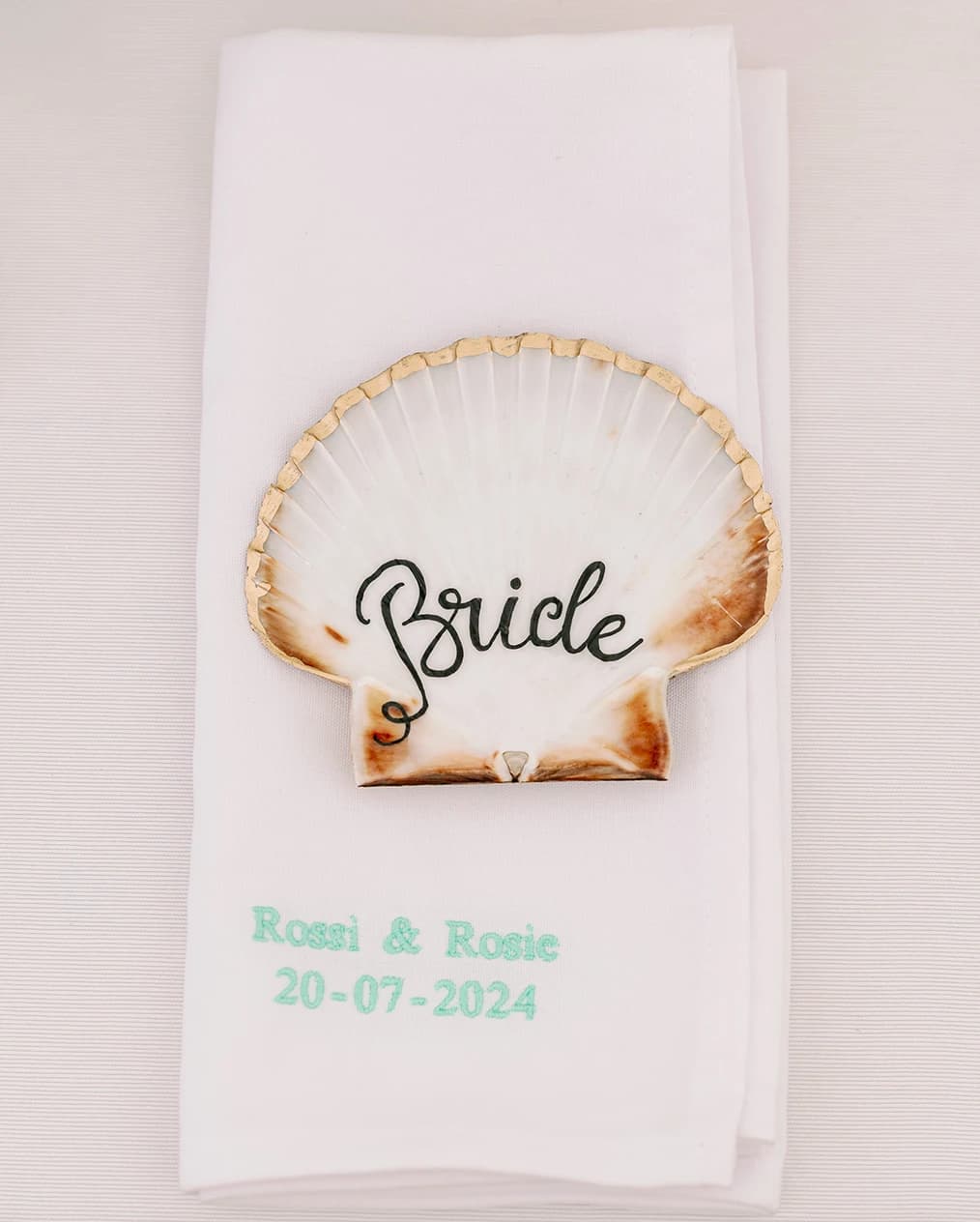An elegant wedding napkin with shell-shapes table placecard with "Bride" handwritten on it 