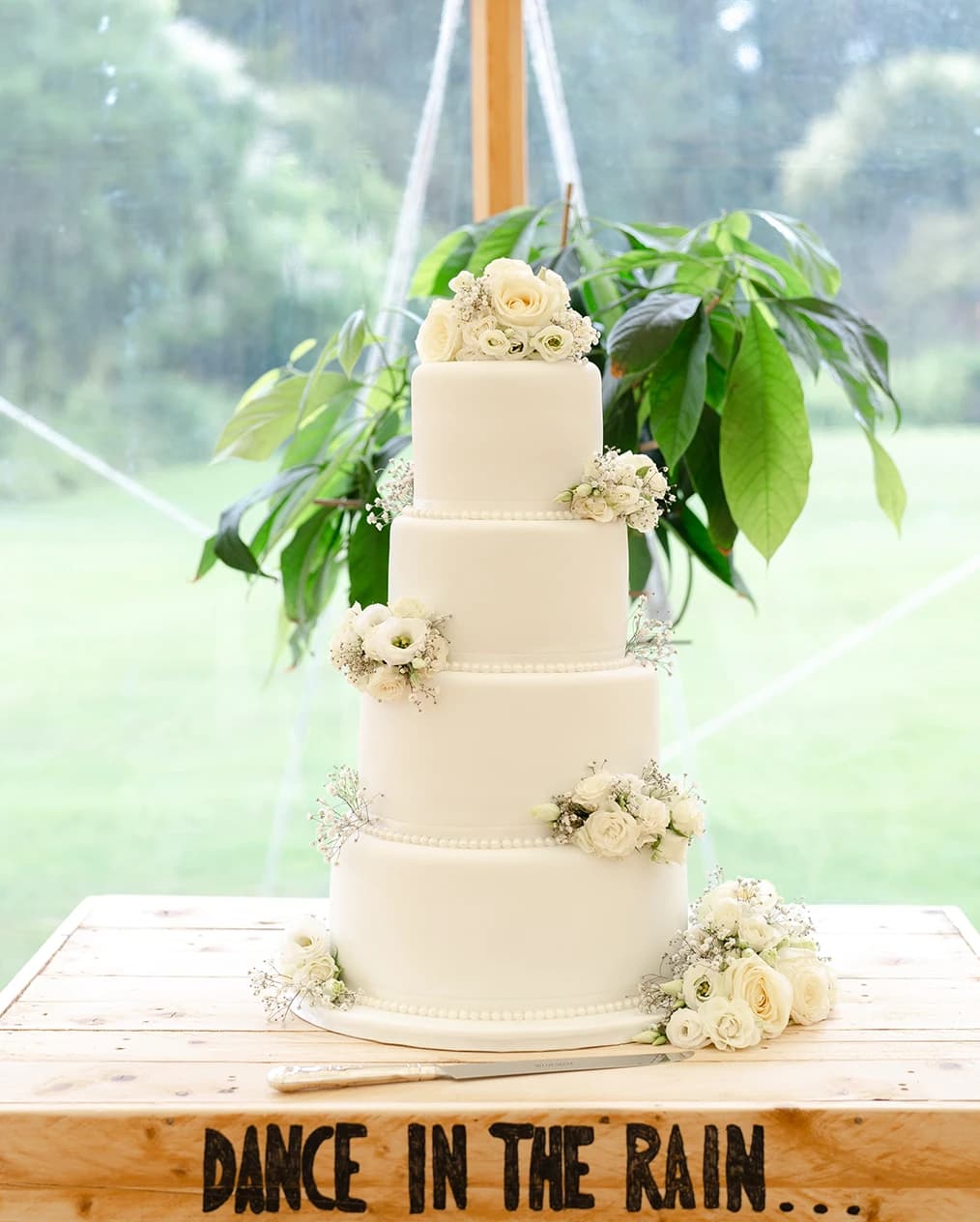 A three tier wedding cake placed on a table with writing "Dance in the rain"