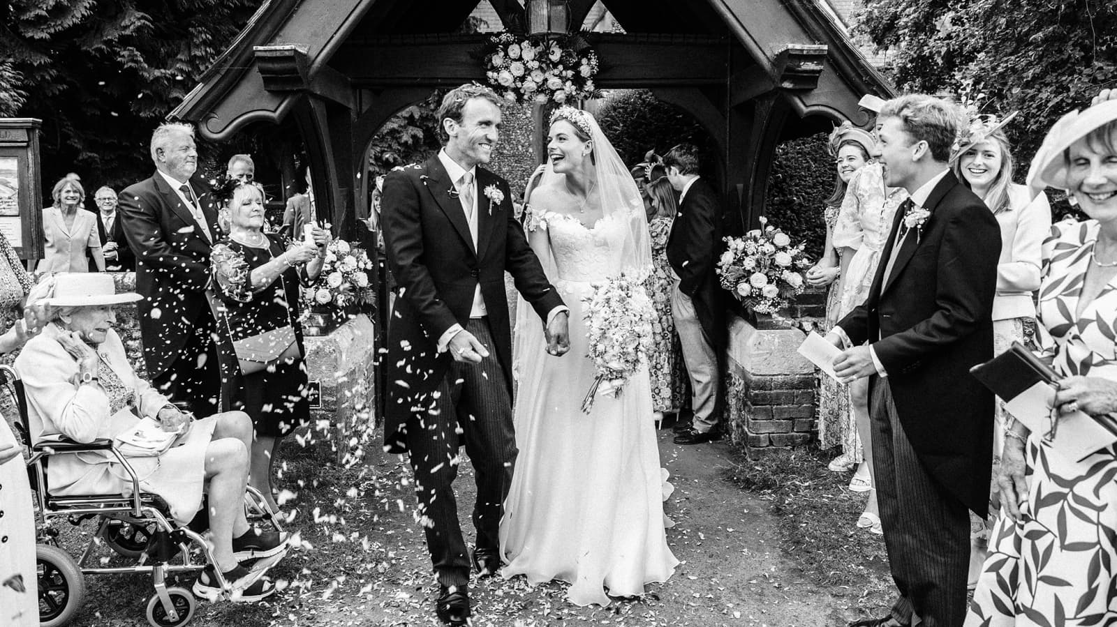 Newlywed groom and bride walk out of the church, with confetti being thrown by guests