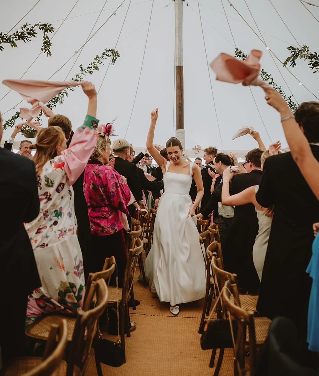 Bride entering the marquee as guests wave pink napkins in celebration