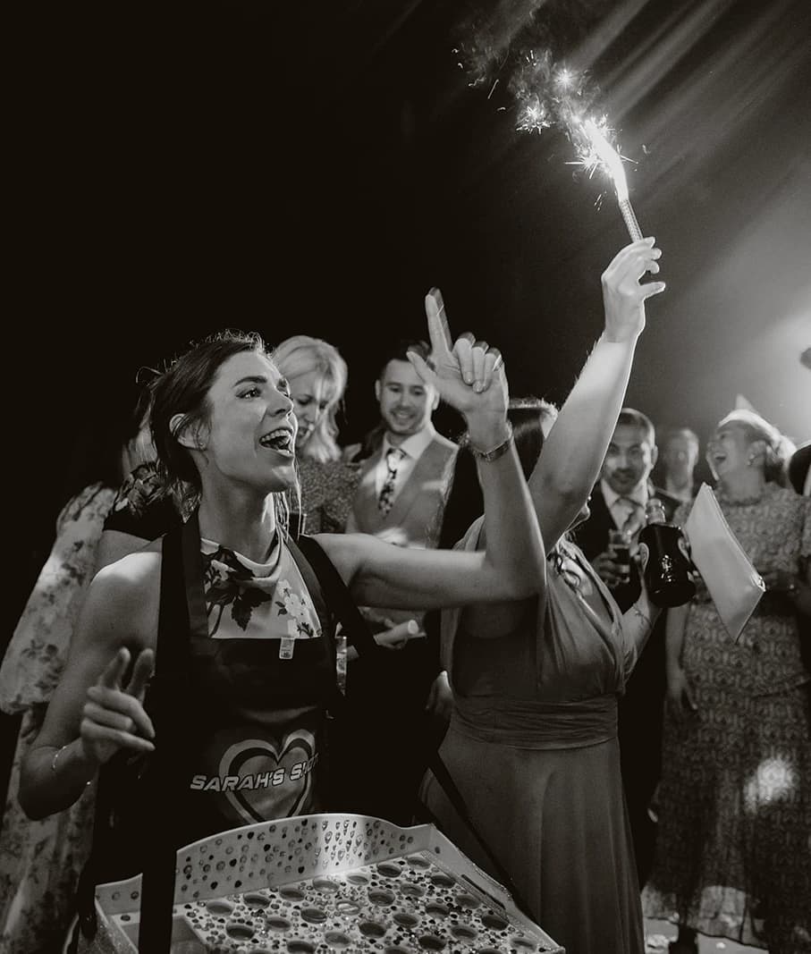 Black and white photograph of the bridesmaid serving shots with a sparkler