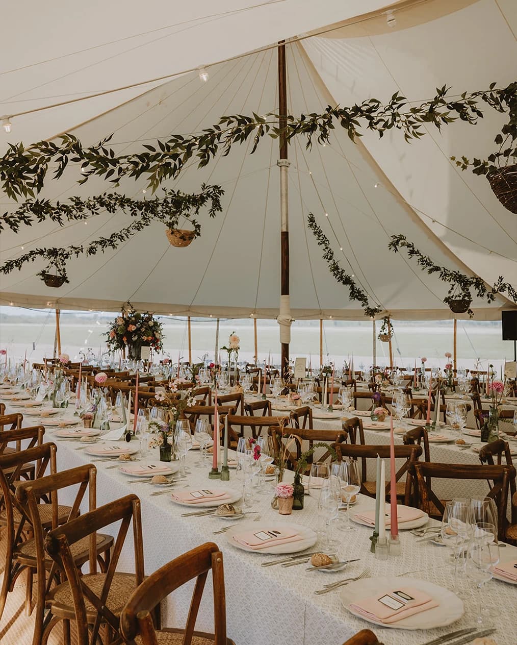 Hanging foliage garland and pink flowers above guests at the round bar in the marquee