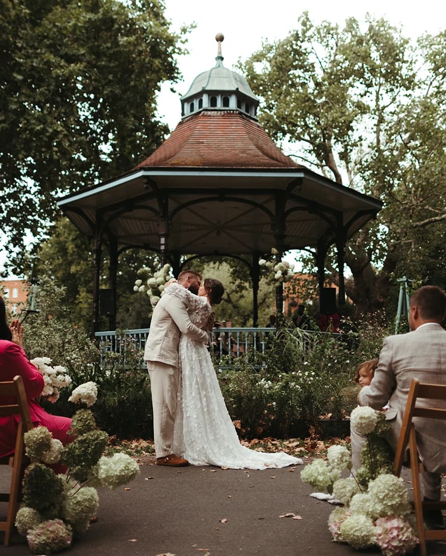 Bride and groom kiss during their wedding ceremony in front of park gazebo